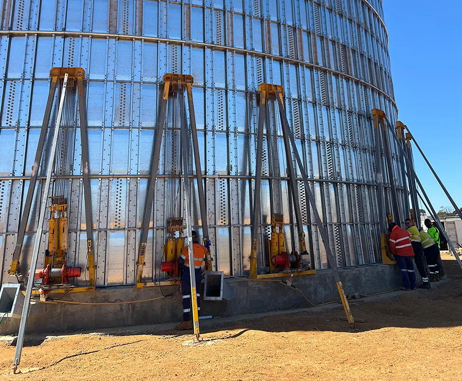 Large metal storage silo with workers at the base learning in training program in Perth, Western Australia